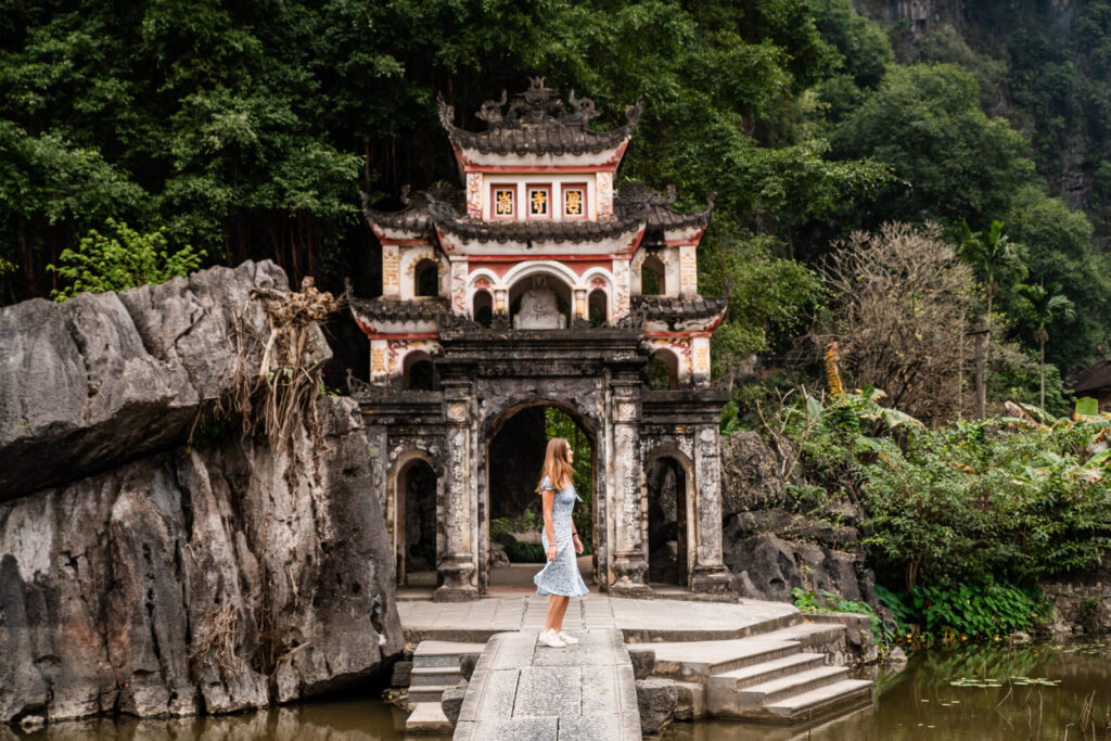Premium Photo  Lone tourist with traditional vietnamese hat at bich dong  pagoda entrance gate, ninh binh vietnam, buddhist temple set amid jungle  and karst mountain range. traveling alone, keep social distancing.