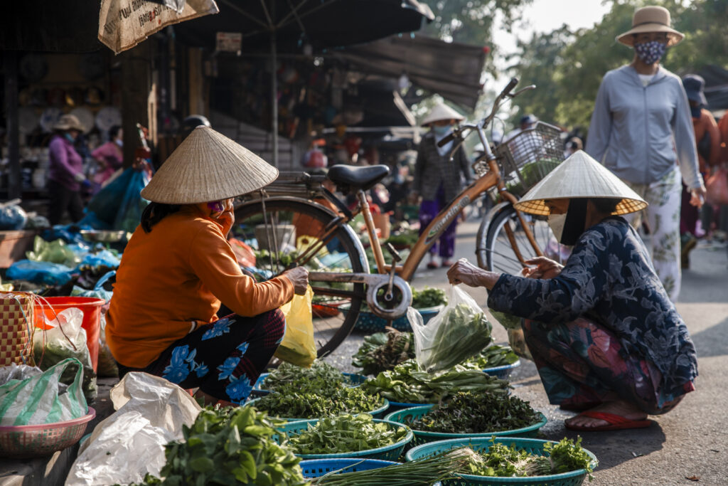 Woman in conical hat buying veggies at central market in Hoi an