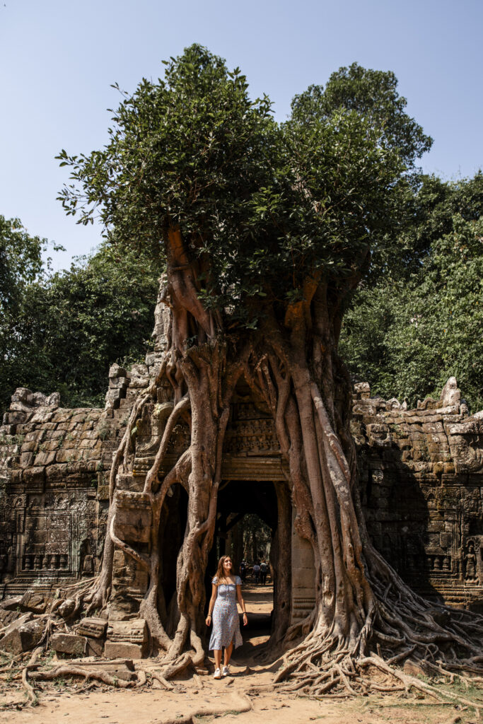 Girl standing underneath strangler fig tree that has taken over the entrance of Ta Som Temple in Angkor, Cambodja 